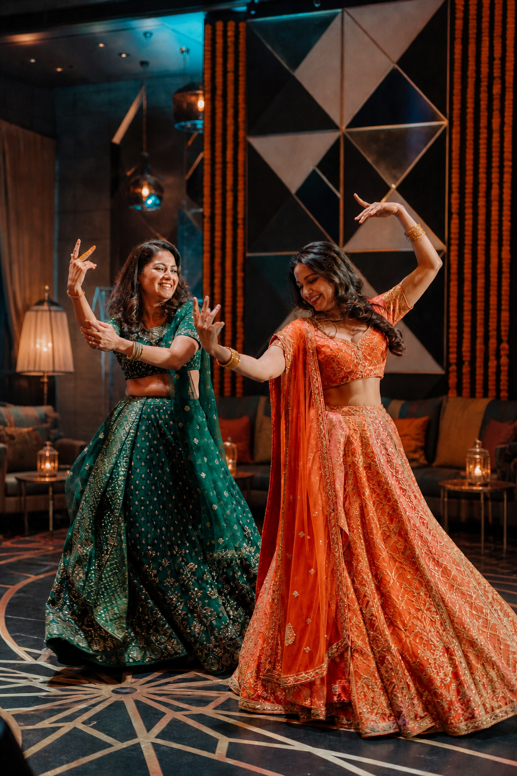 Two women performing a choreographed sangeet dance in contrasting jewel-tone lehengas